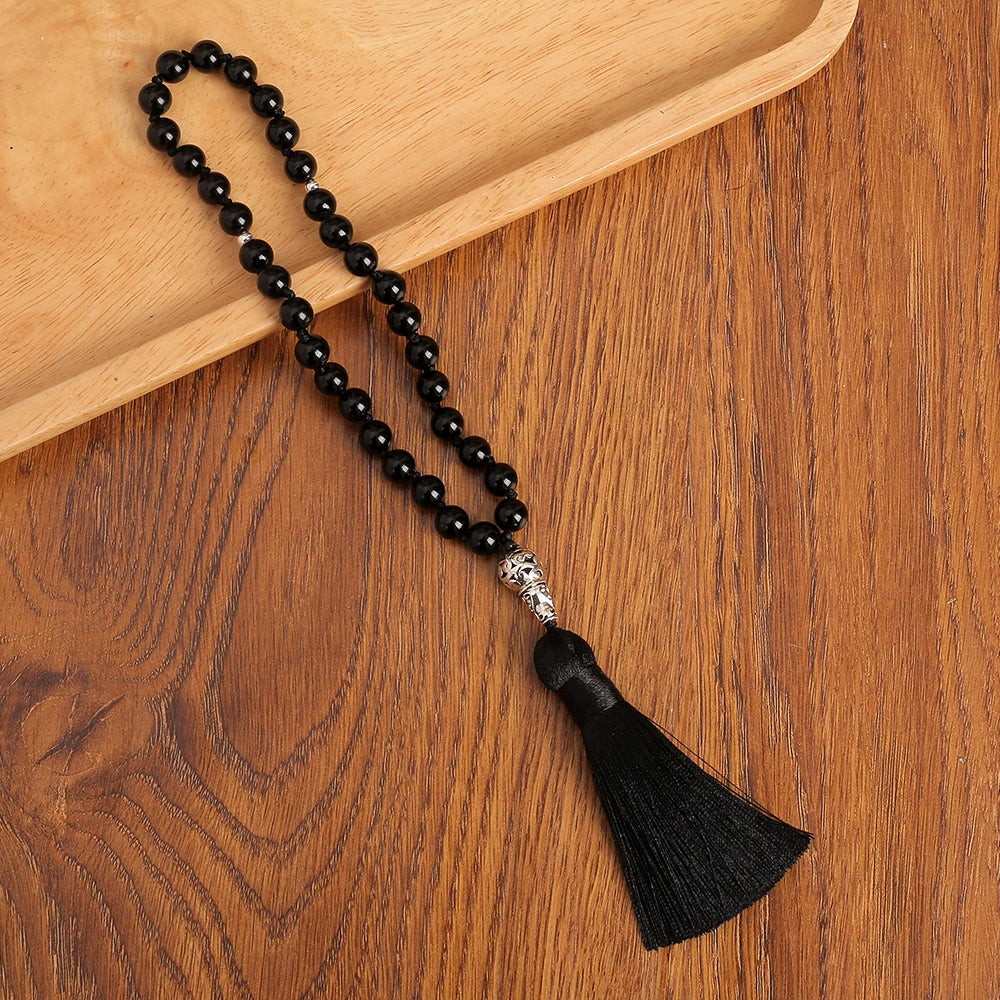 Black onyx beaded prayer beads with a tassel on a wooden surface