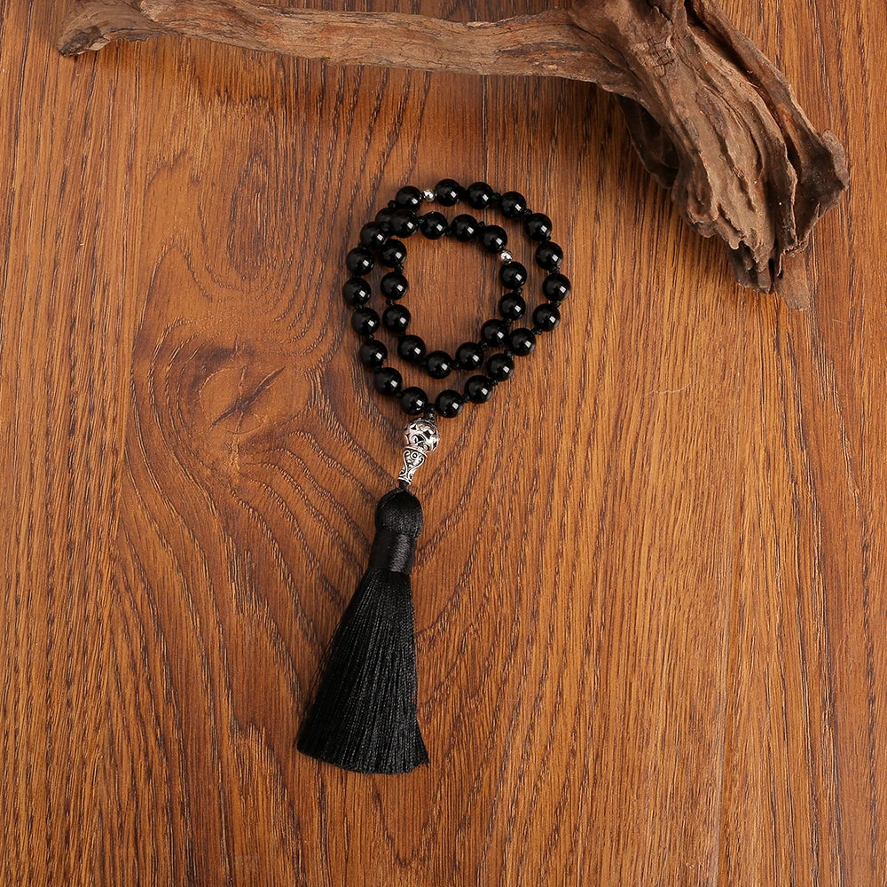 Black beaded onyx prayer beads with a tassel on a wooden surface