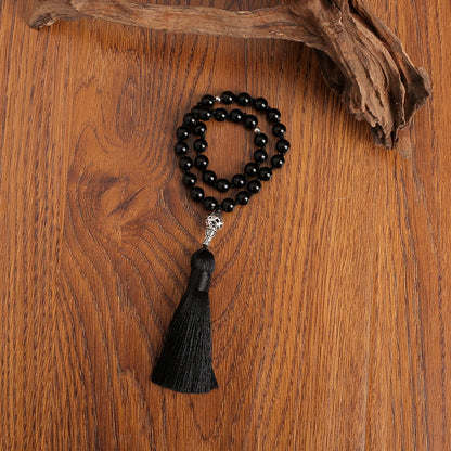 Black beaded onyx prayer beads with a tassel on a wooden surface