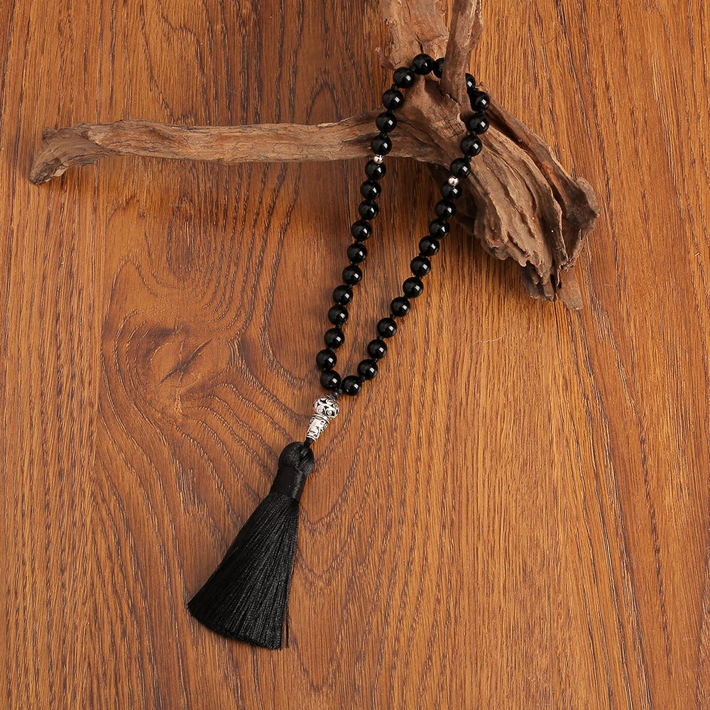 Black beaded onyx knotted prayer beads with a tassel on a wooden surface