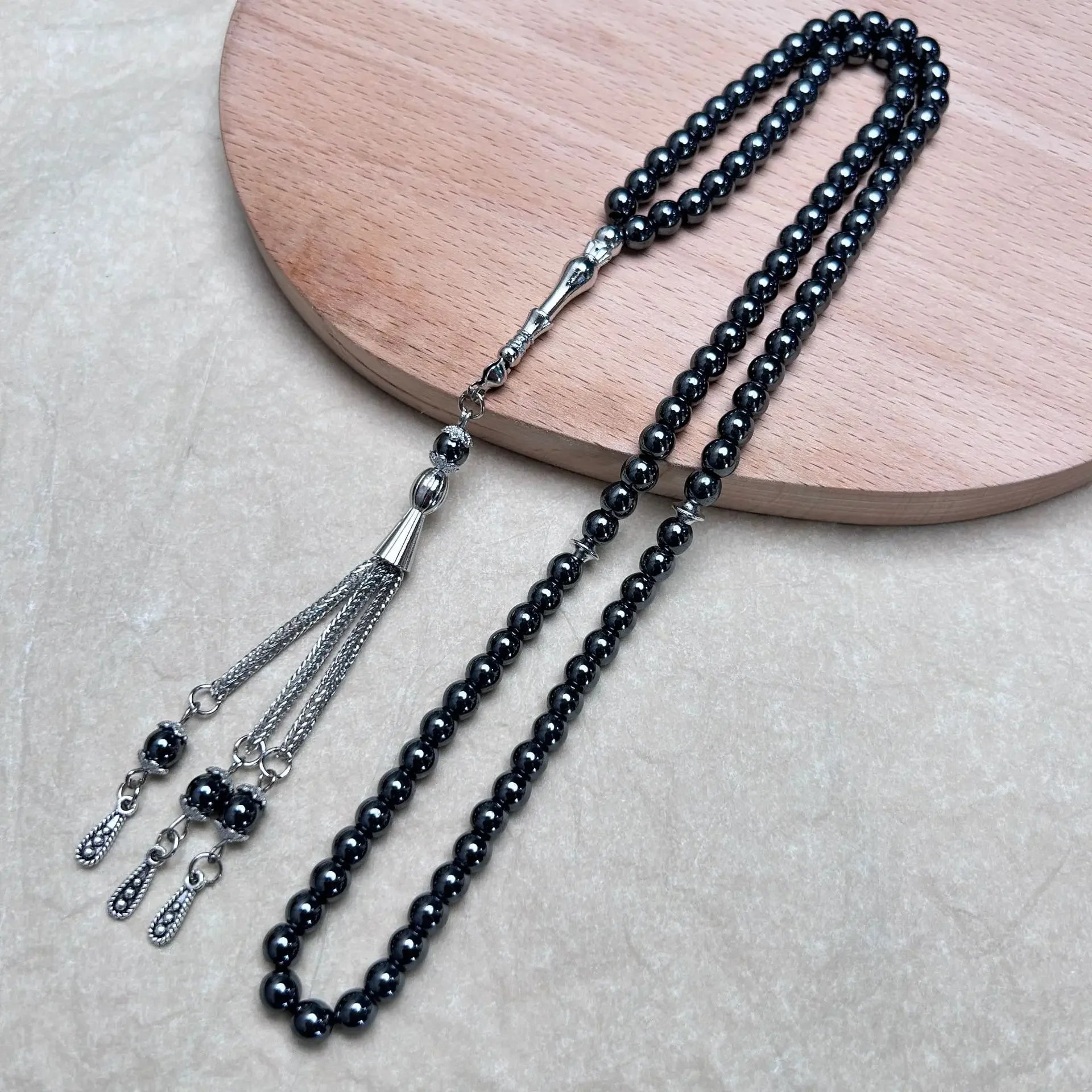 Hematite tasbih with metal tassel arranged on wooden board